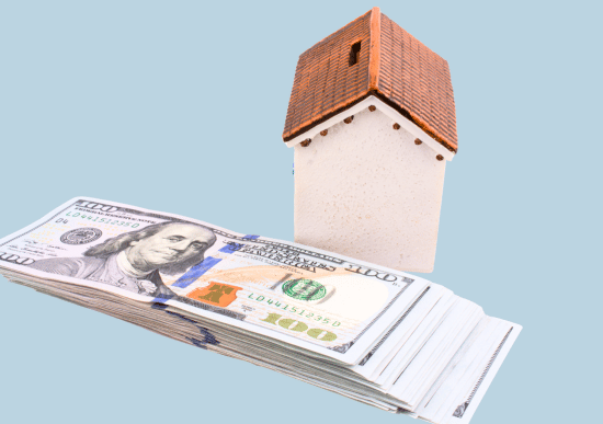 Stack of US $100 bills sits before a small white house with a brick roof, symbolizing wealth, real estate, and financial investment.